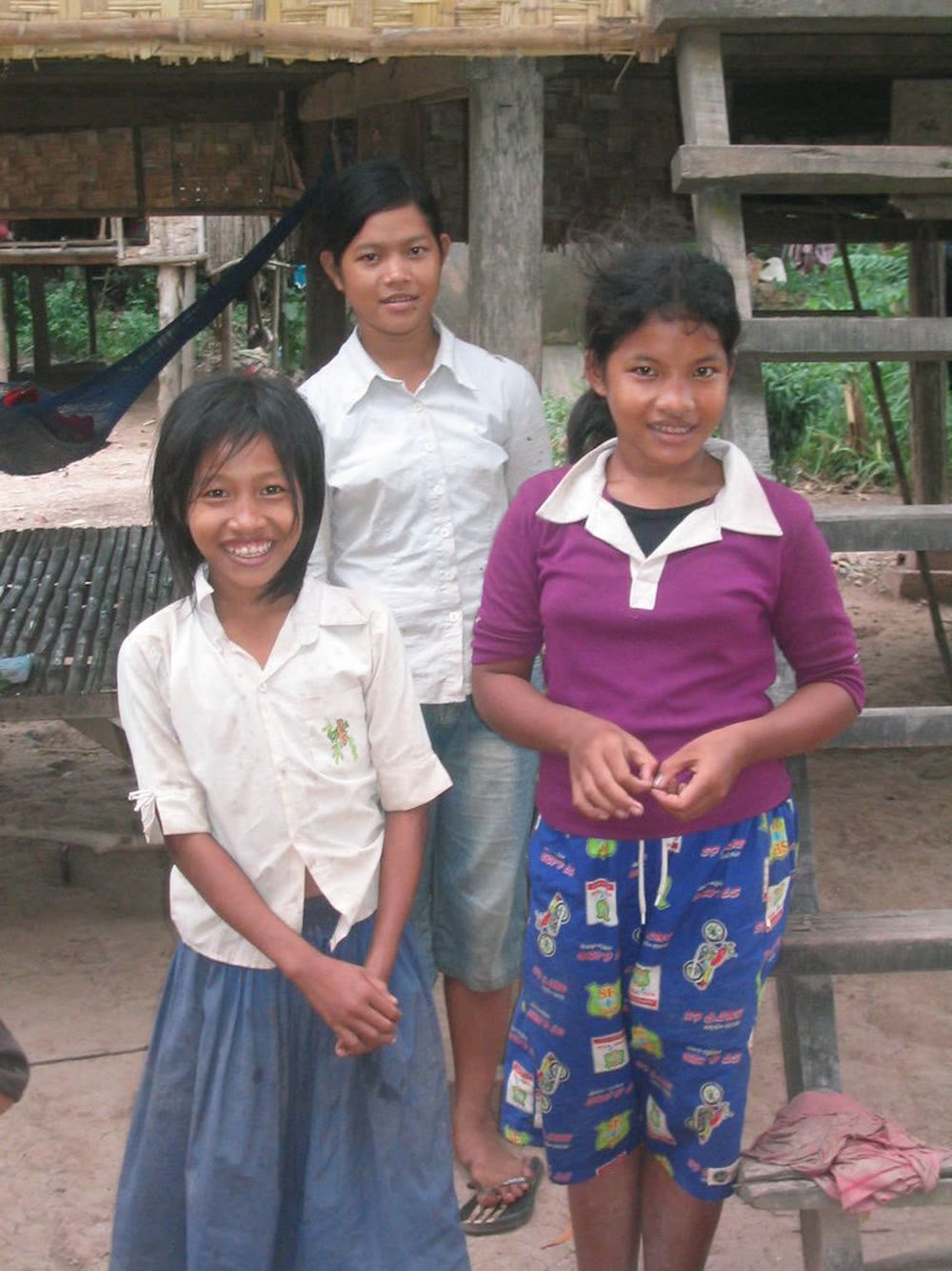 Three young students standing together, smiling, outside their school
